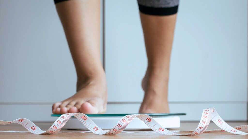Woman,Foot,Stepping,On,Weigh,Scales,With,Tape,Measure,In